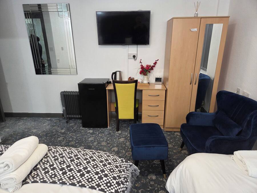 Camera d'albergo con un letto, una scrivania con una sedia, una televisione, un armadio e un termosifone.