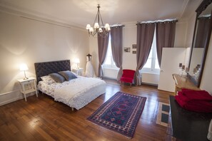 A bedroom with a large bed, a nightstand, a red armchair, a dresser, and a mirror. - Maison des 7 Lieux (Chablis)