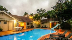 Una piscina con sillas de descanso y un tobogán, rodeada de edificios y vegetación.