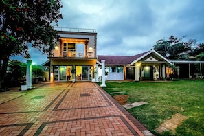 Uma casa de dois andares com calçada pavimentada, varanda coberta e gramado bem cuidado.