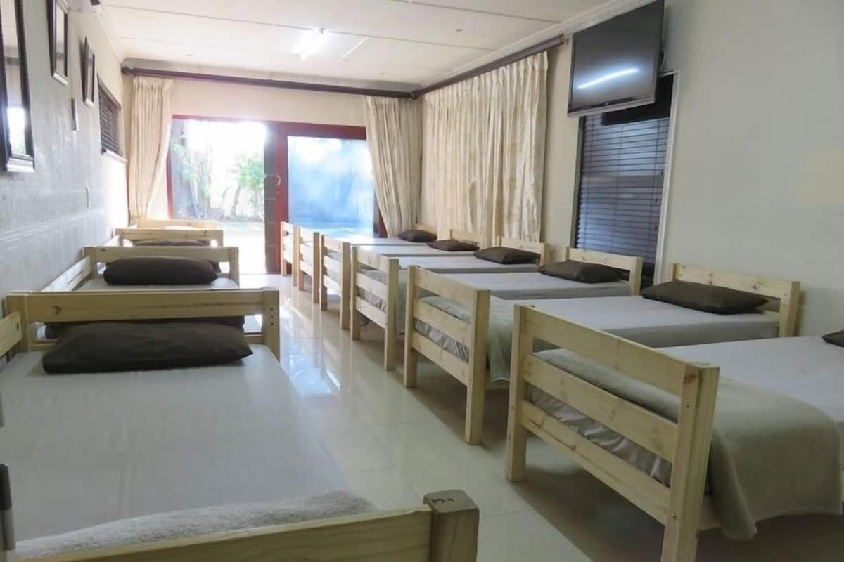 A dormitory room with wooden beds, a television, and a window with curtains.