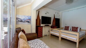 Una habitación acogedora con un sofá, una cama con cabecero de madera, un televisor y un cuadro con barcos.