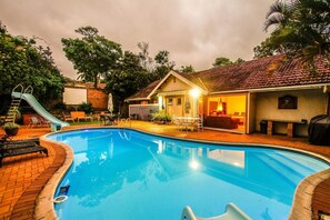 A swimming pool with a slide, surrounded by a patio area with outdoor furniture and a covered seating area. - Umhlanga Backpackers (Umhlanga)