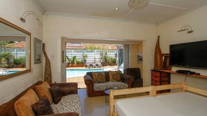 Habitación de hotel con cama, sofá, televisión, mesita de madera y vista a una piscina.