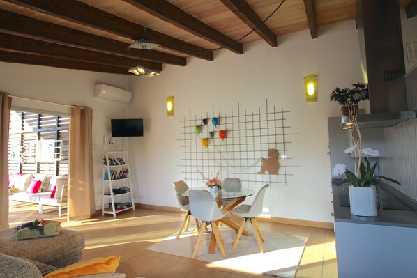 Een moderne woonkamer met een glazen eettafel, witte stoelen, een boekenkast en een aan de muur bevestigde televisie.