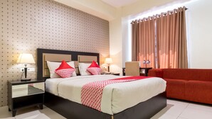 A hotel room with a large bed, two bedside tables with lamps, a red sofa, and a window with curtains. - OYO Flagship 1348 Hotel Home Anaya (Medan)