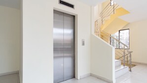 A modern interior with a metallic elevator, a staircase with yellow accents, and a large window providing natural light. - OYO Flagship 1348 Hotel Home Anaya (Medan)
