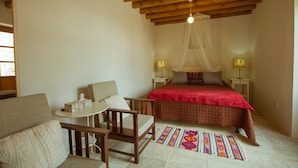 Ein gemütliches Schlafzimmer mit einem Bett, einem kleinen Tisch, zwei Stühlen, einem farbenfrohen Teppich und einer Holzbalkendecke.