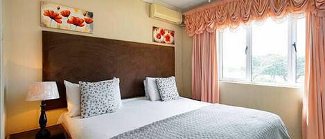 Quarto de hotel com uma cama grande, mesa de cabeceira com abajur, ventoinha no teto e obras de arte nas paredes.