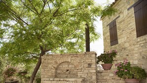A stone structure with a brick archway, surrounded by potted plants and a tree. - Thyone Uno Cottage (Vavla)