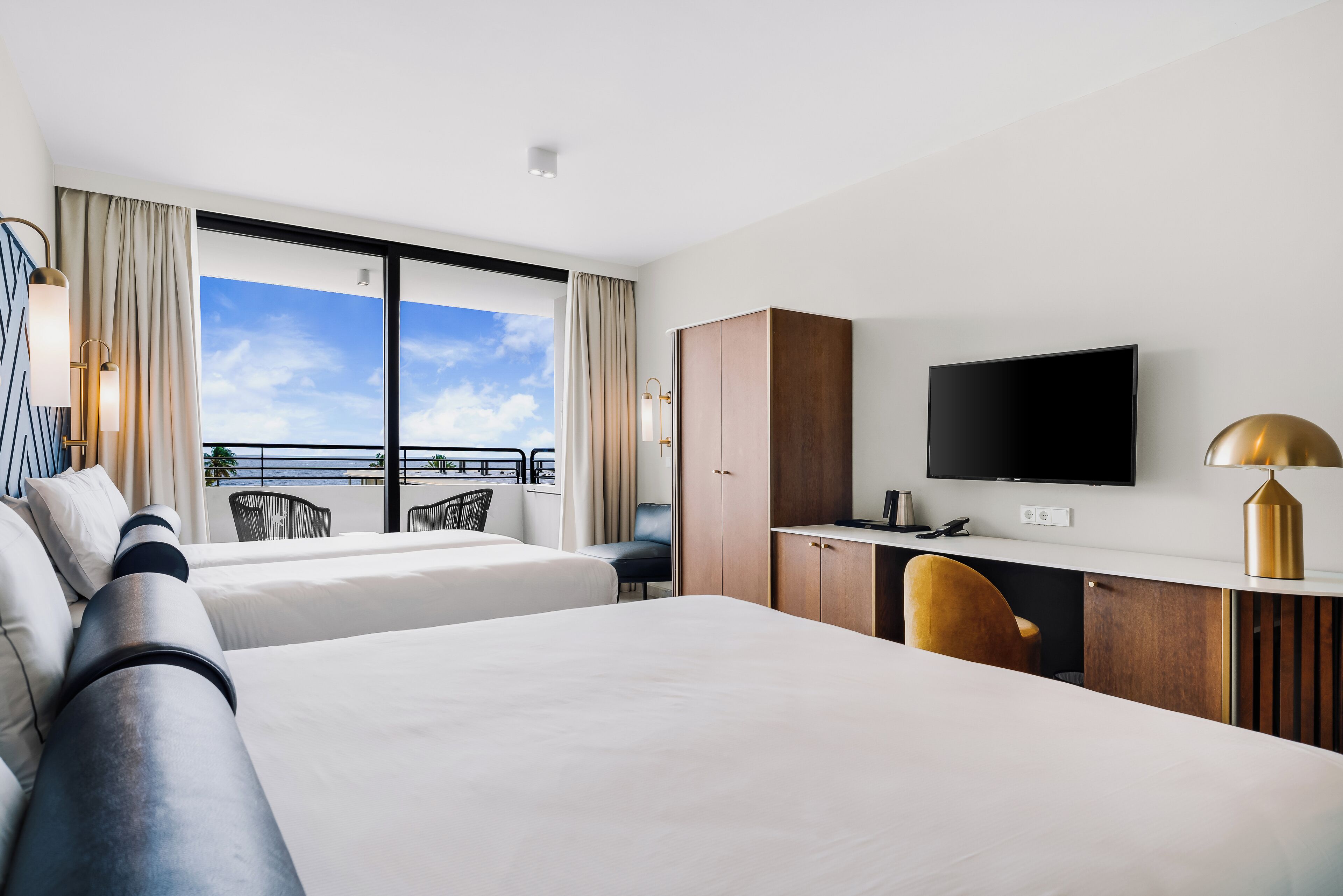 Habitación de hotel con dos camas, un escritorio, un televisor y un balcón con vistas.