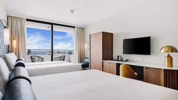 Habitación de hotel con dos camas, un escritorio, un televisor y un balcón con vistas.