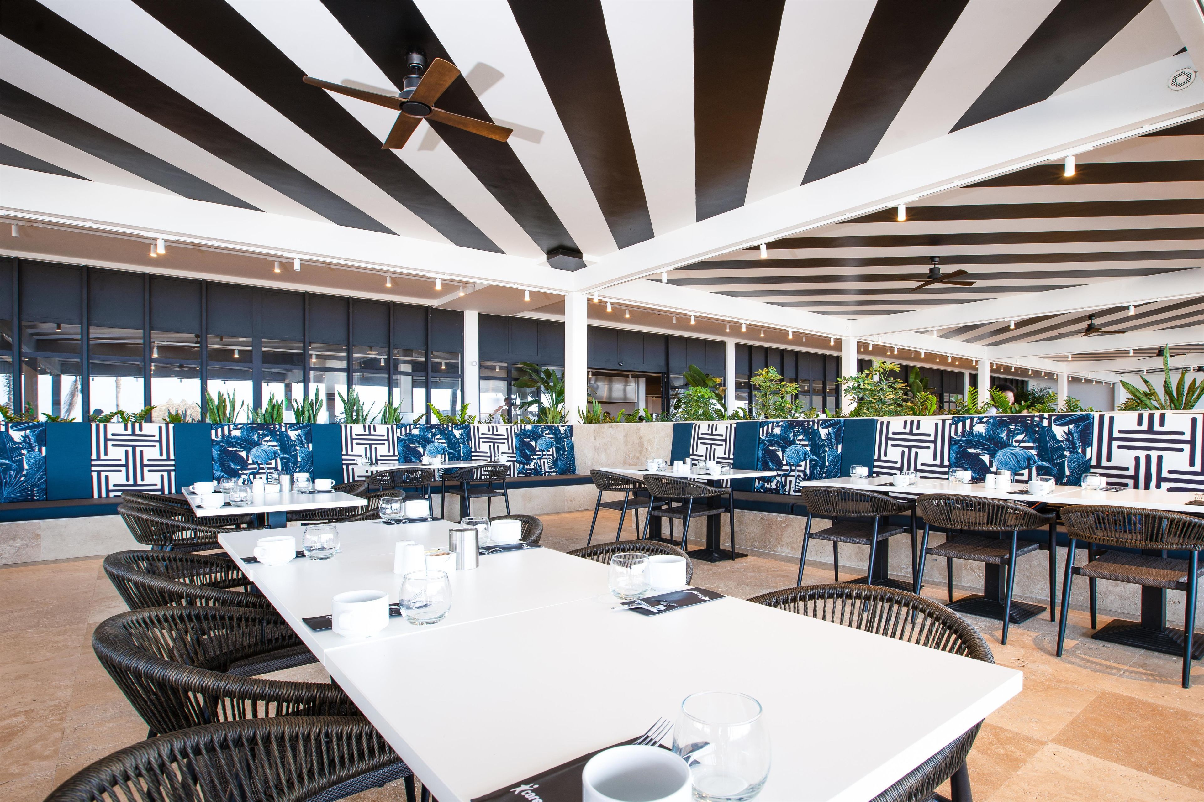 An outdoor dining area with tables and chairs, ceiling fans, and decorative wall panels.