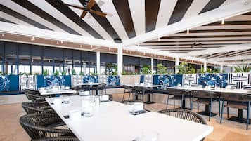 An outdoor dining area with tables and chairs, ceiling fans, and decorative wall panels.