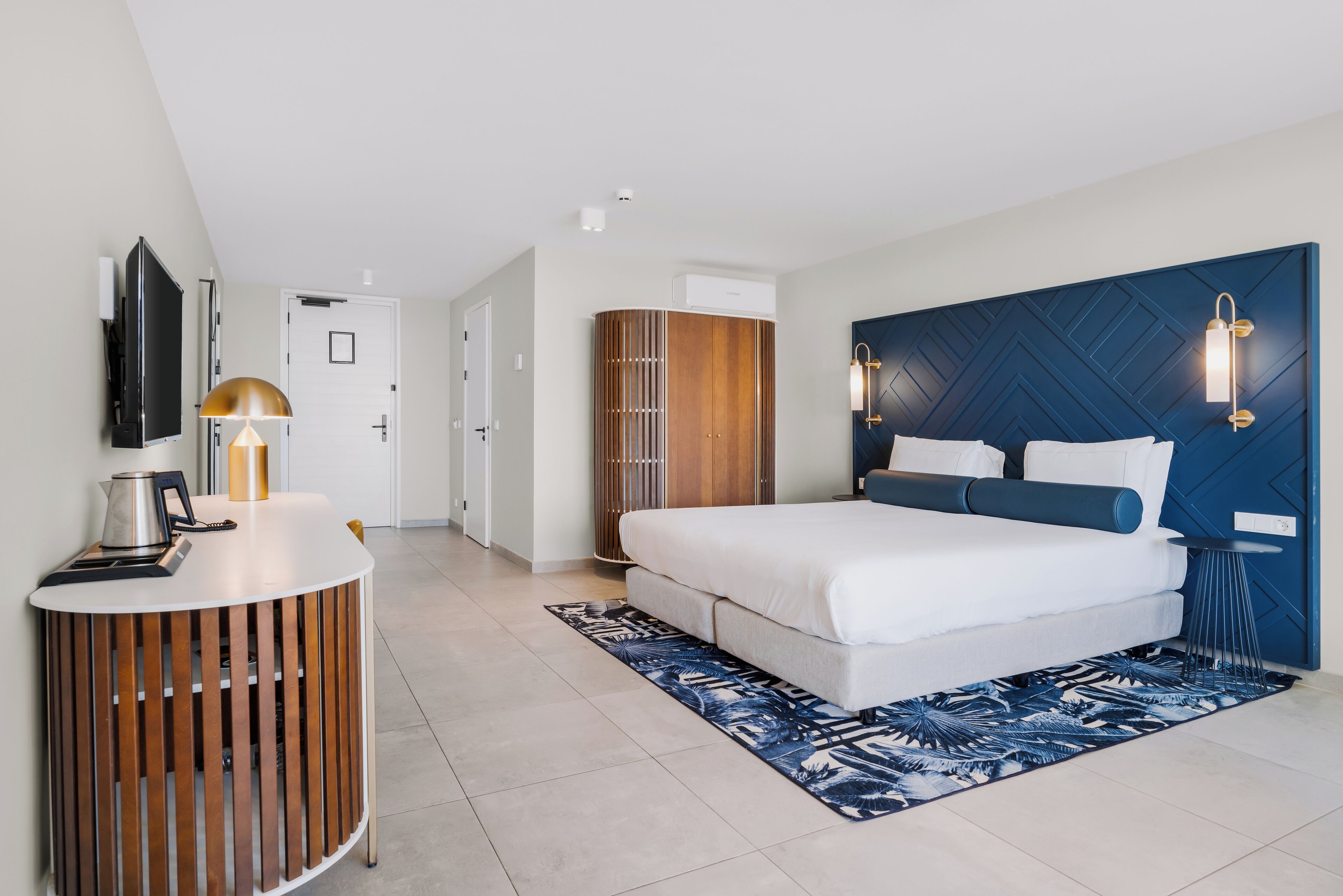 Une chambre d’hôtel moderne équipée d’un lit, d’une table de chevet en bois, d’une télévision et d’une armoire.