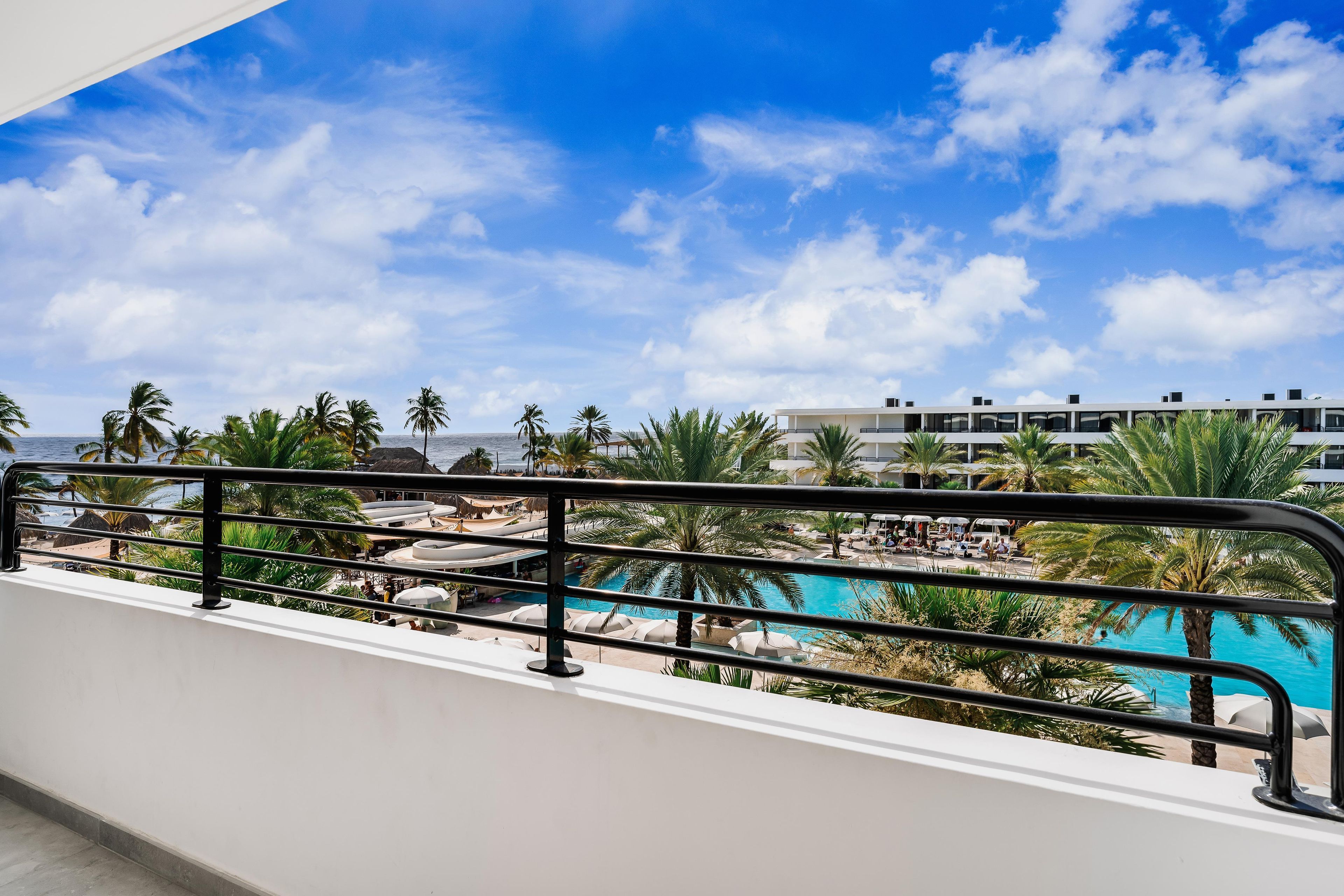A poolside view with a clear sky, palm trees, and a modern building in the background.