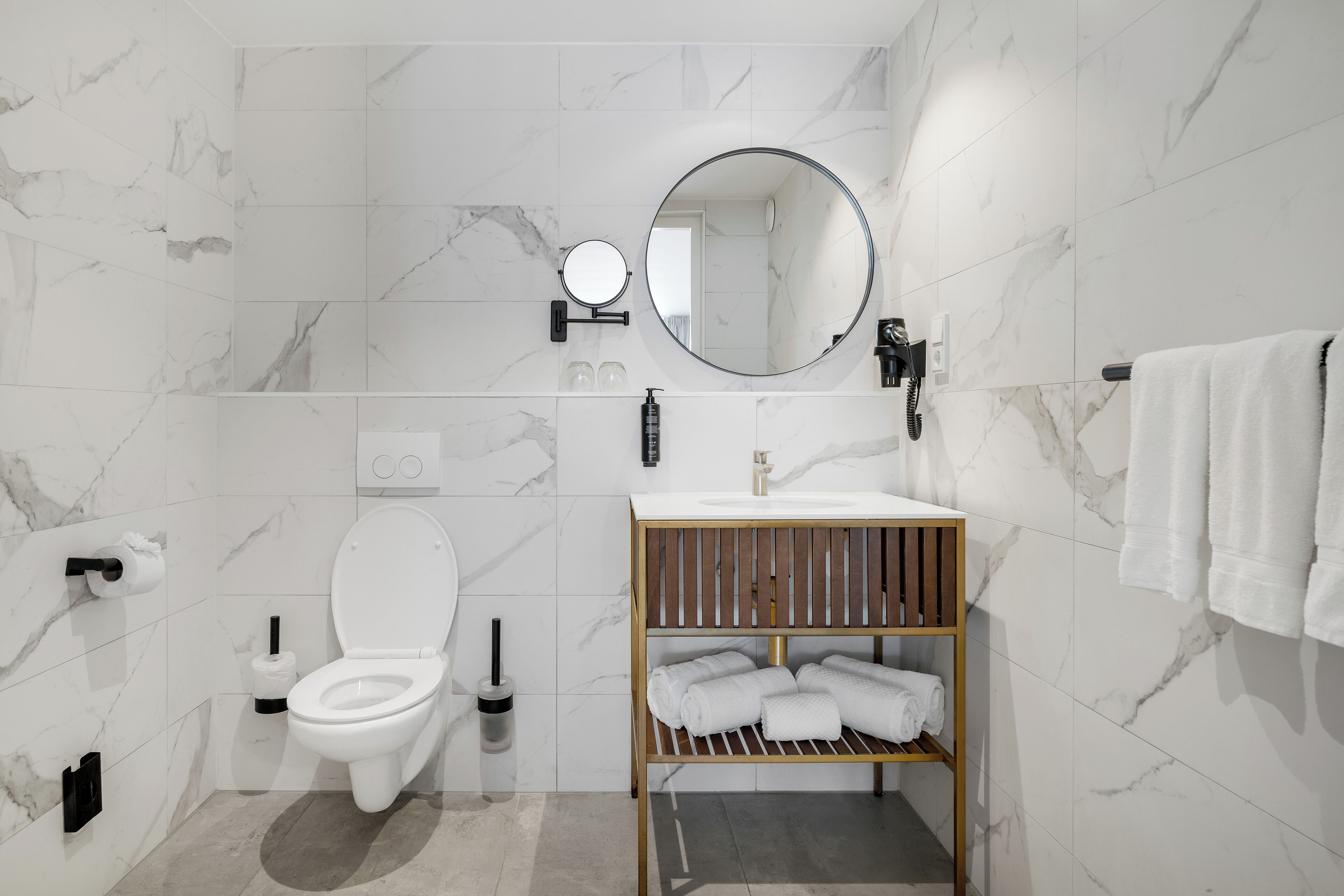 Een moderne badkamer met een witte marmeren wand, een houten wastafelmeubel met een wastafel, een toilet en een handdoekhouder.