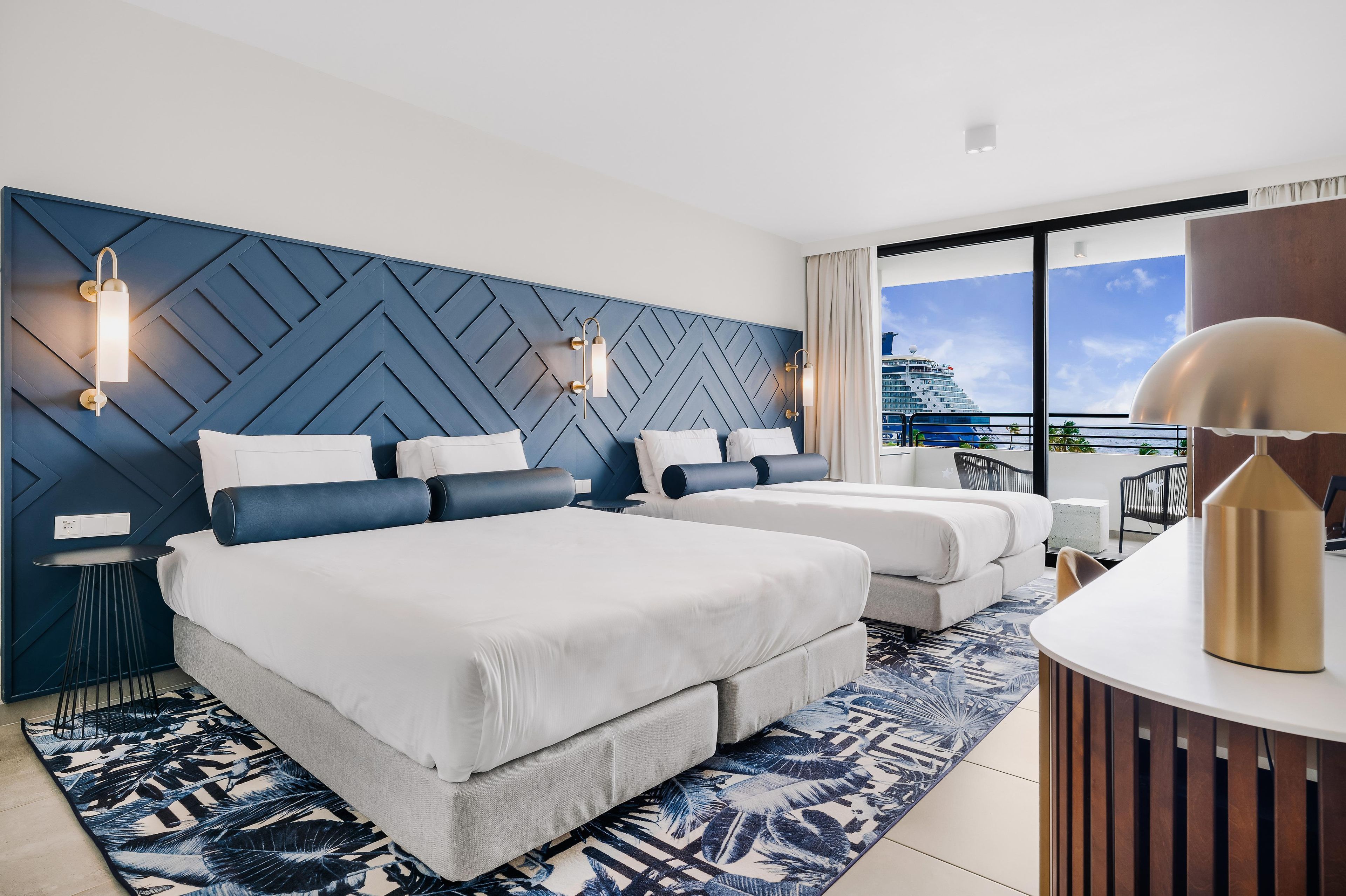 Habitación de hotel con dos camas, un ventanal con vista a un crucero y un diseño moderno en la pared.