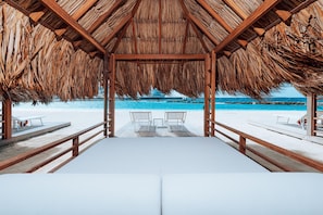 A beach cabana with a thatched roof, white cushioned seating, and a view of the ocean. - Mangrove Beach Corendon Curacao All-Inclusive Resort, Curio by Hilton (Willemstad)