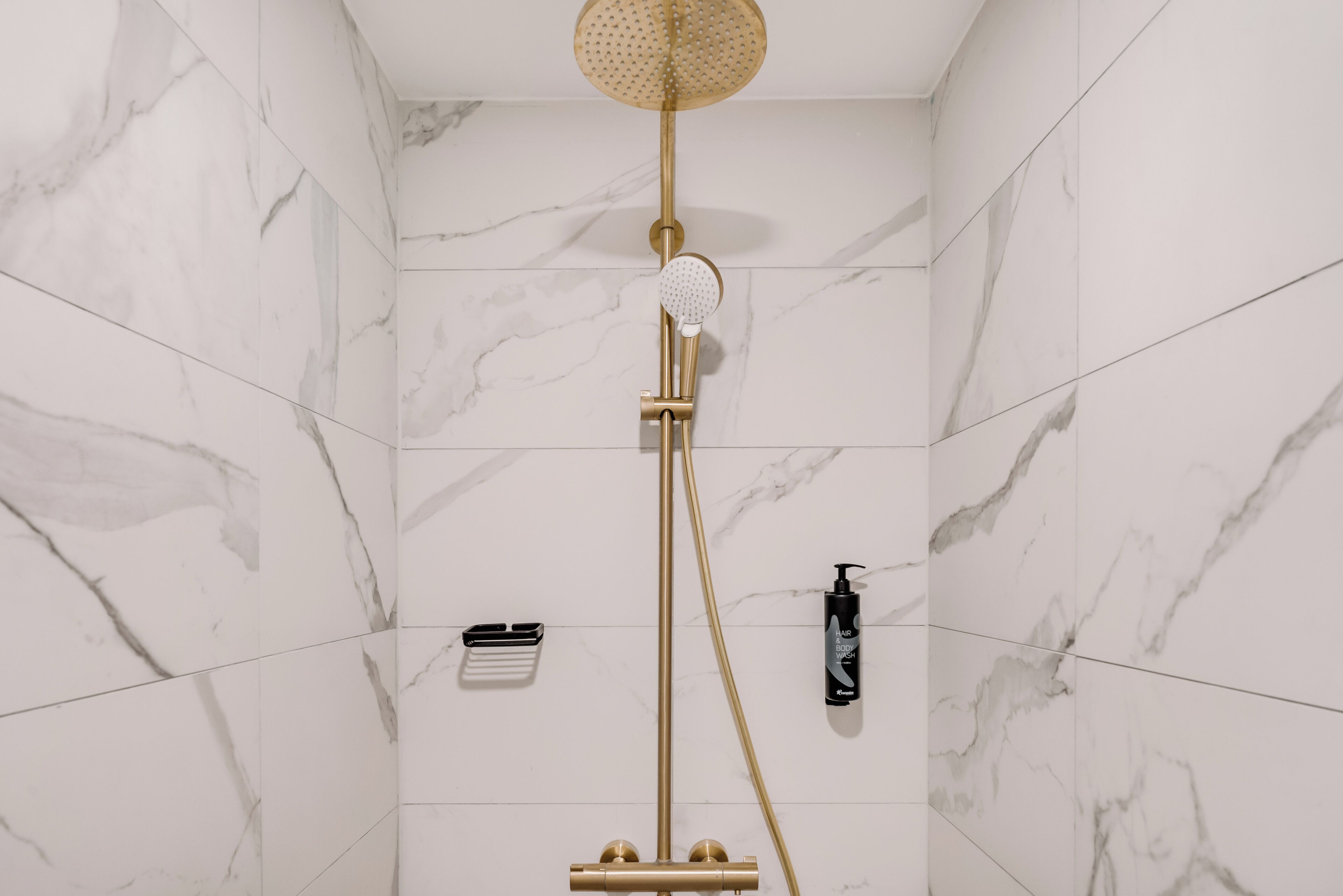 Un baño con ducha de oro, paredes de mármol y una botella de jabón de cuerpo.