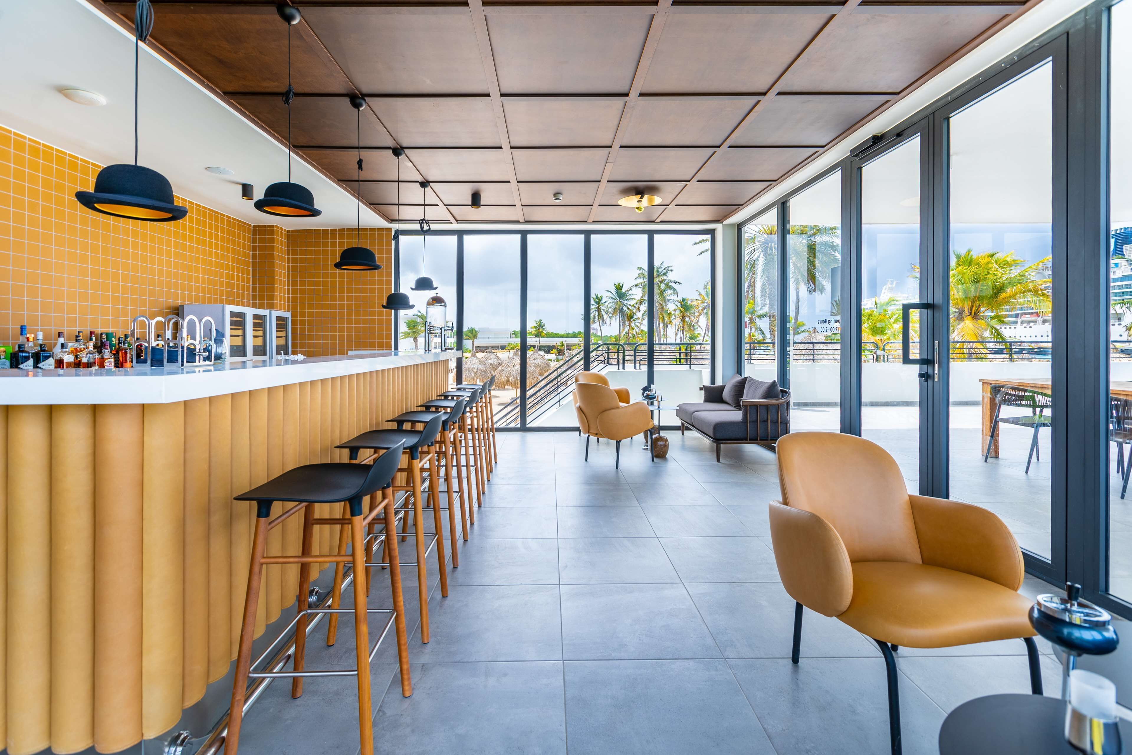 Un'area bar moderna con un lungo bancone, diversi sgabelli e un angolo salotto con sedie e divano.