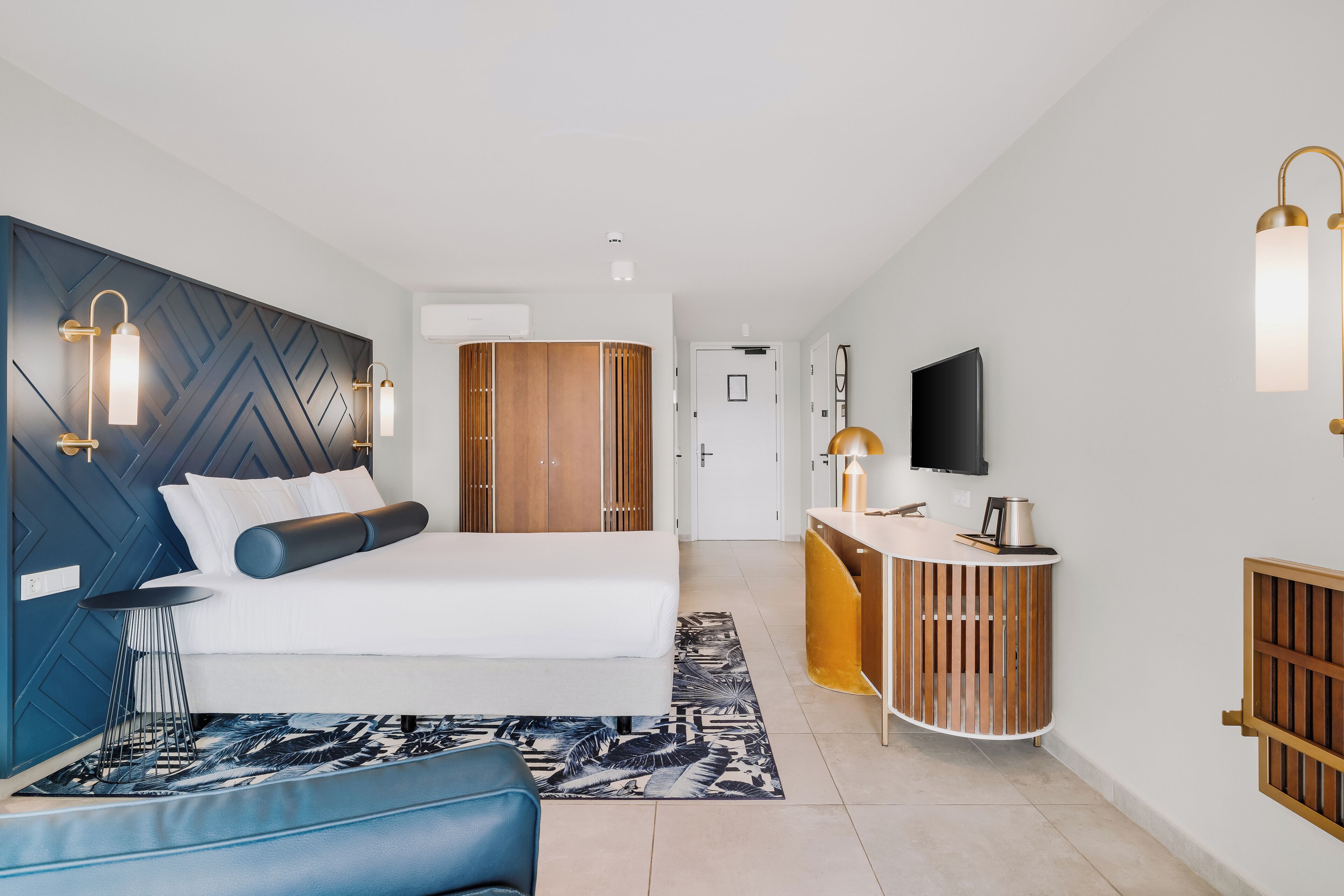 Une chambre d’hôtel moderne équipée d’un lit, d’un bureau, d’une télévision et d’une armoire.