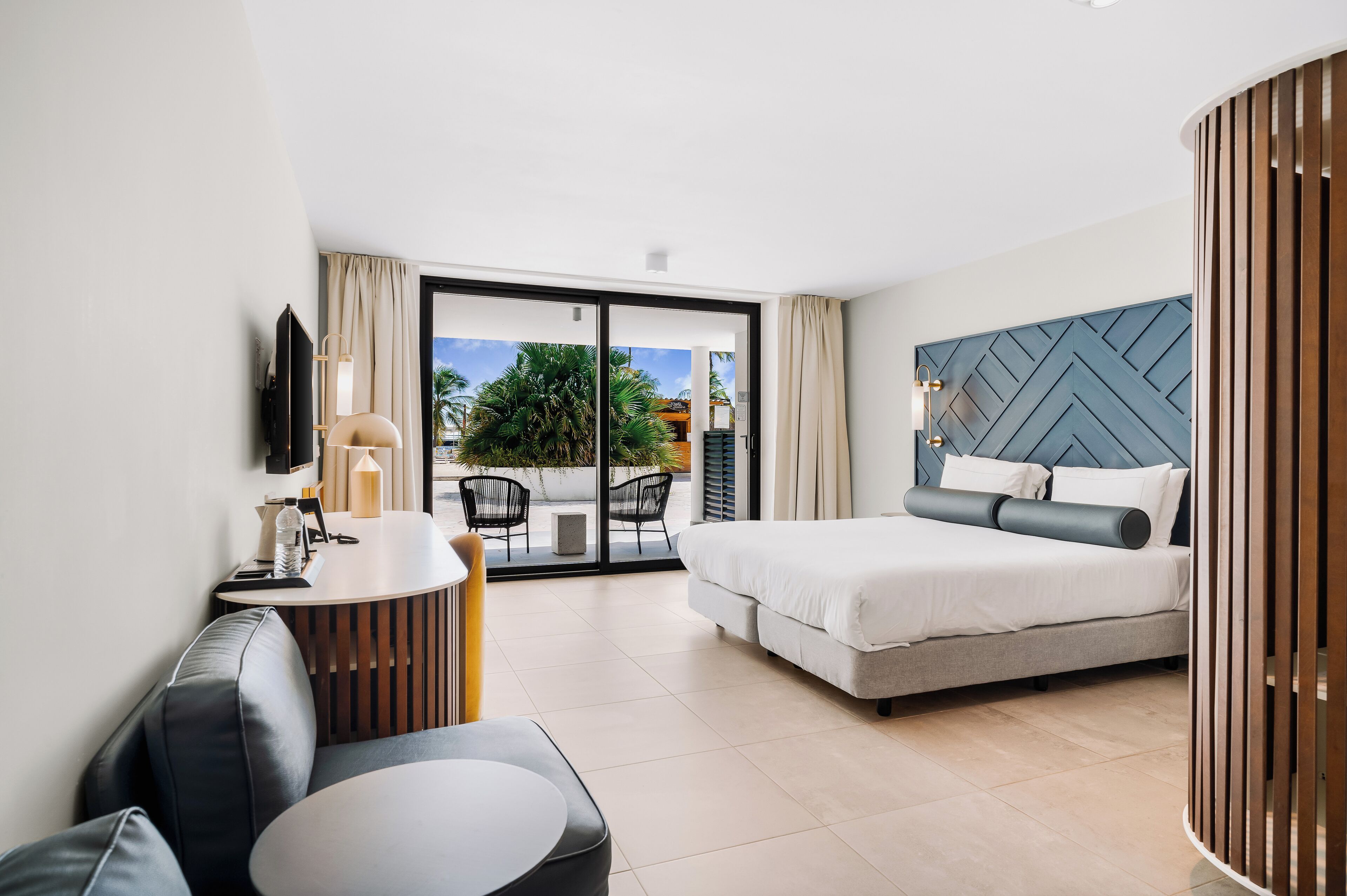 Habitación de hotel moderna con una cama grande, una zona de estar con una mesa y vistas al exterior.