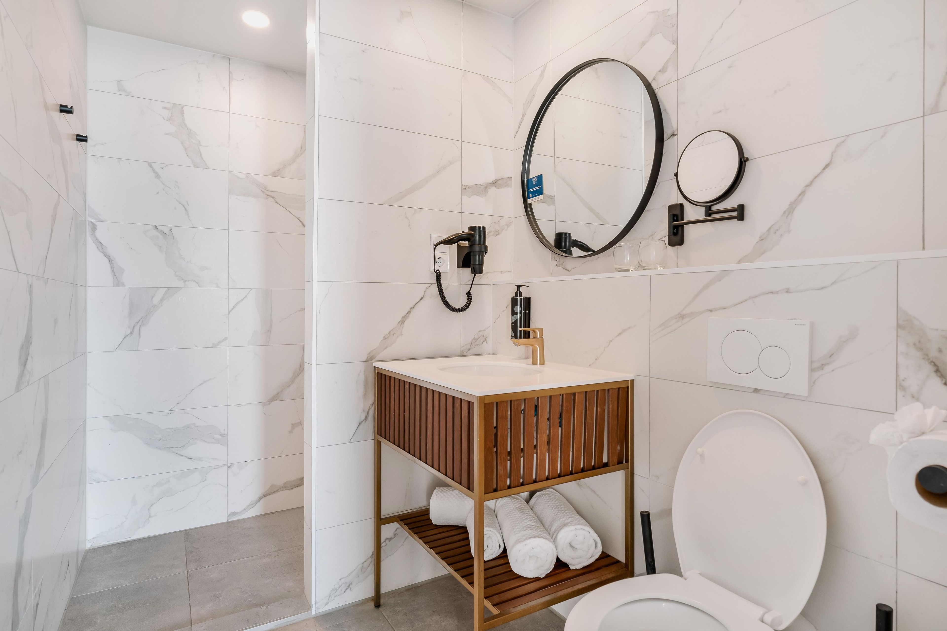 Une salle de bain moderne avec des toilettes blanches, un meuble-lavabo en bois doté d’un miroir et un espace douche.
