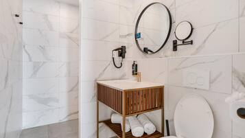 Une salle de bain moderne avec des toilettes blanches, un meuble-lavabo en bois doté d’un miroir et un espace douche.