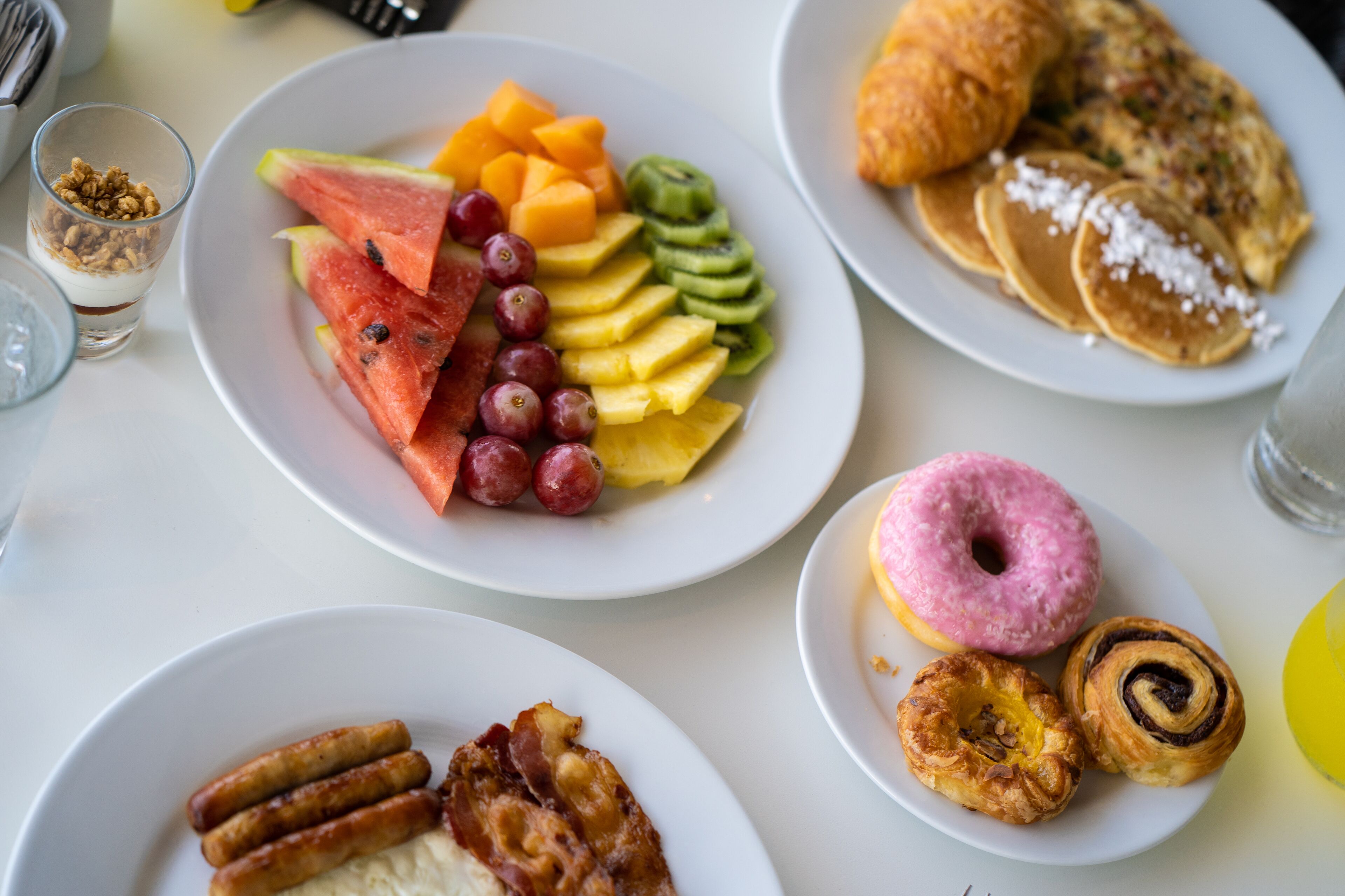 A breakfast spread with various dishes including fruits, pastries, and sausages.