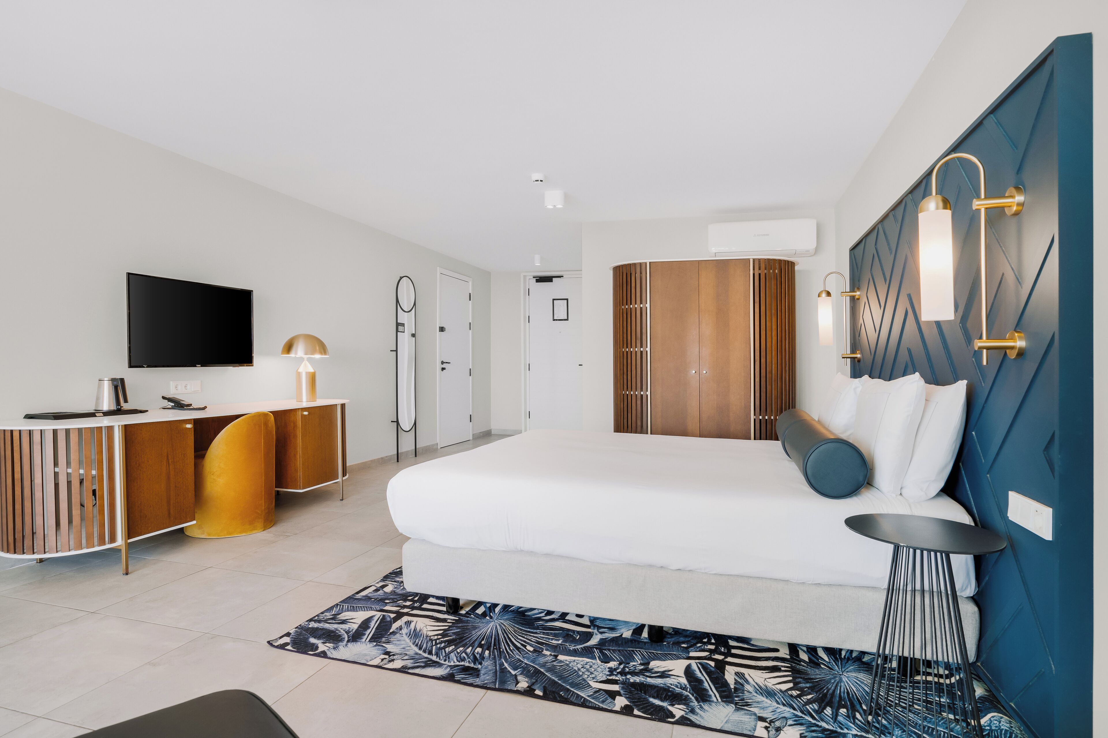 A modern hotel room with a large bed, a desk with a flat-screen TV, a wardrobe, and a bathroom with a shower and toilet.