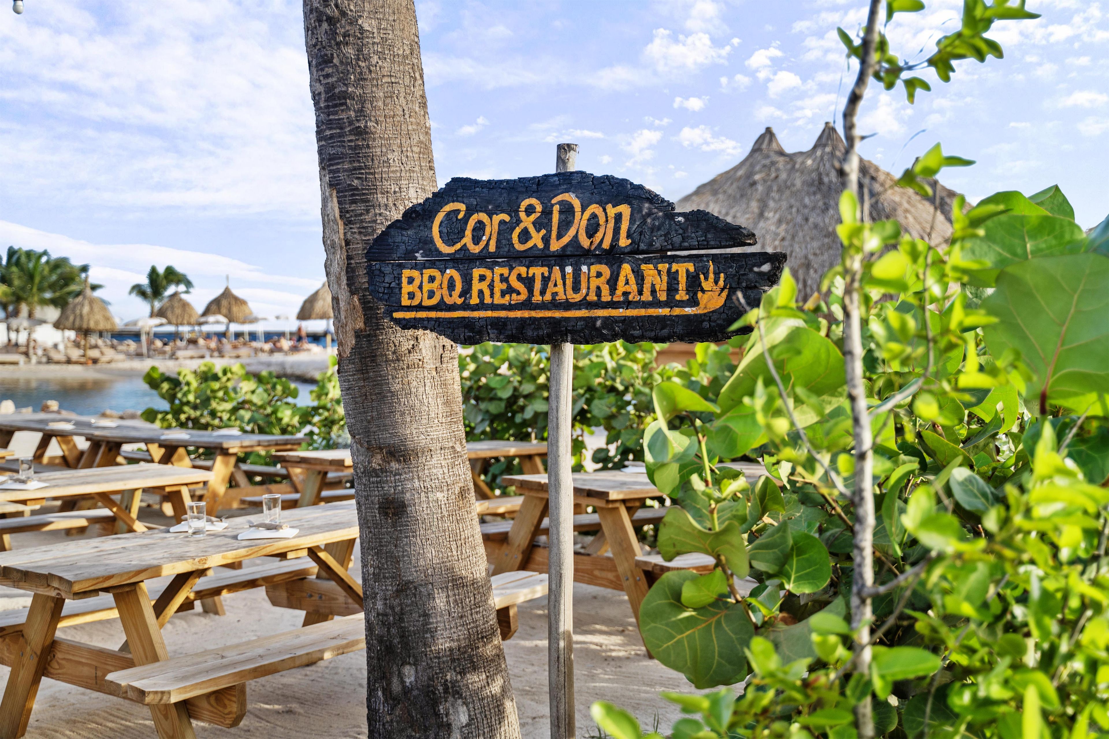 Ein hölzernes Schild mit der Aufschrift 'Cor & Don BBQ Restaurant', das ein Restaurant kennzeichnet.