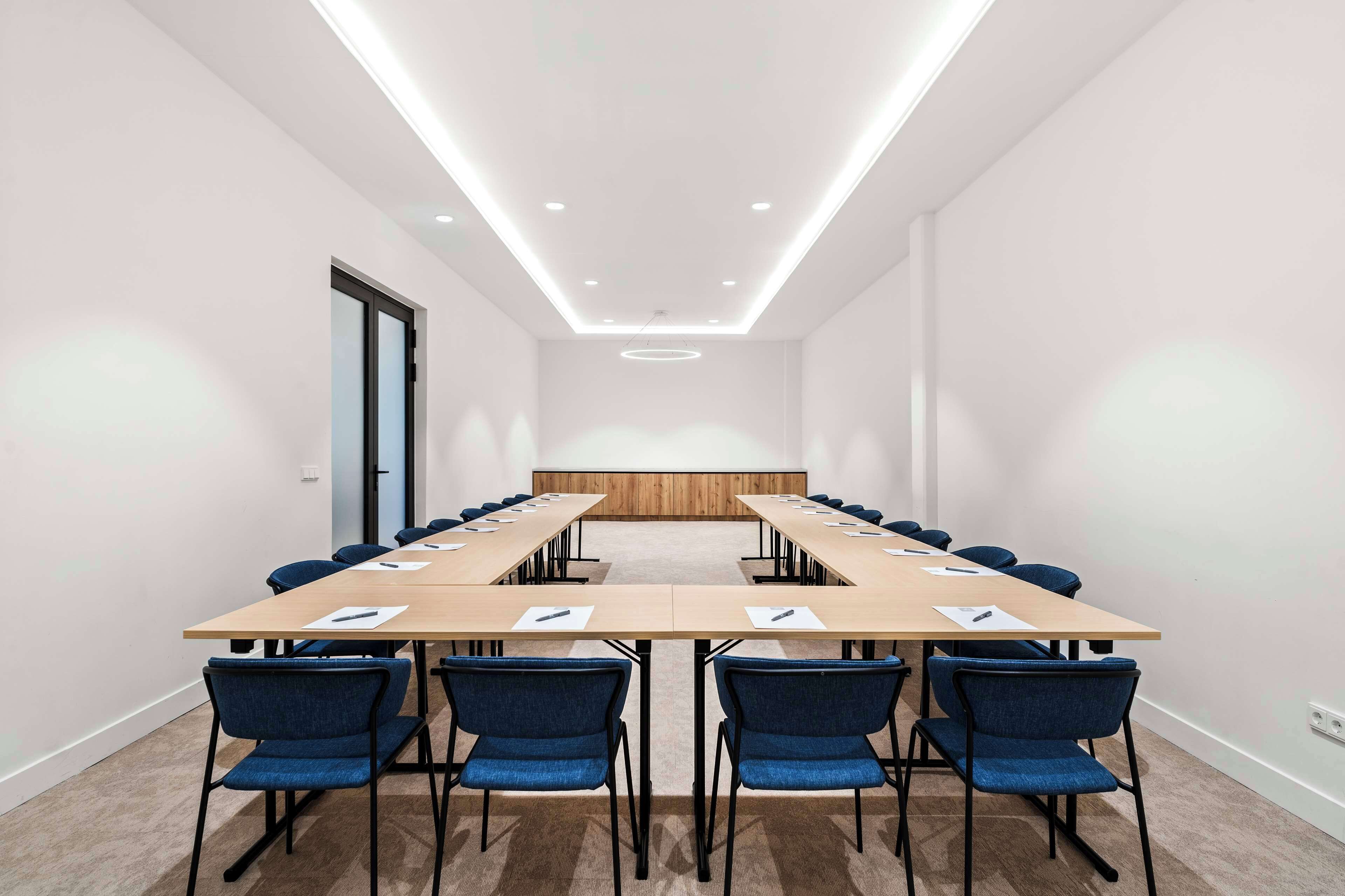 A conference room with a long table, blue chairs, and a wooden panel wall.