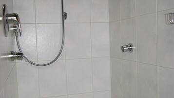 A small, tiled shower area with a handheld showerhead and a wall-mounted faucet.