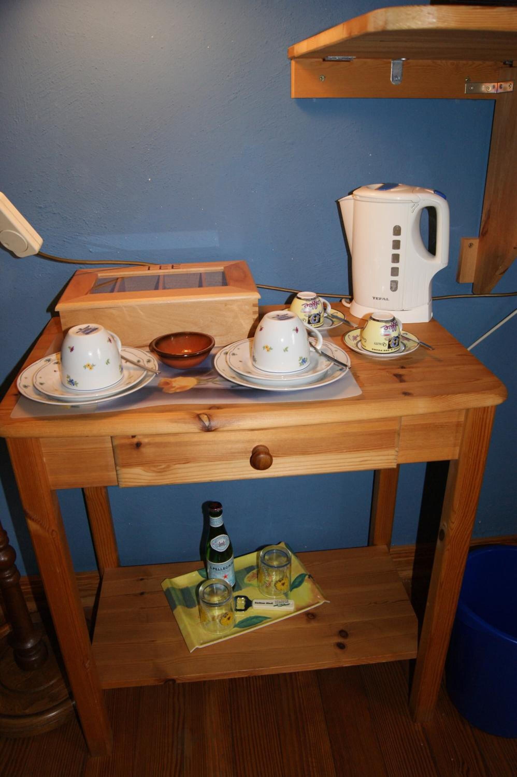 Een klein houten tafeltje met een theeset, een waterkoker en een biertje.