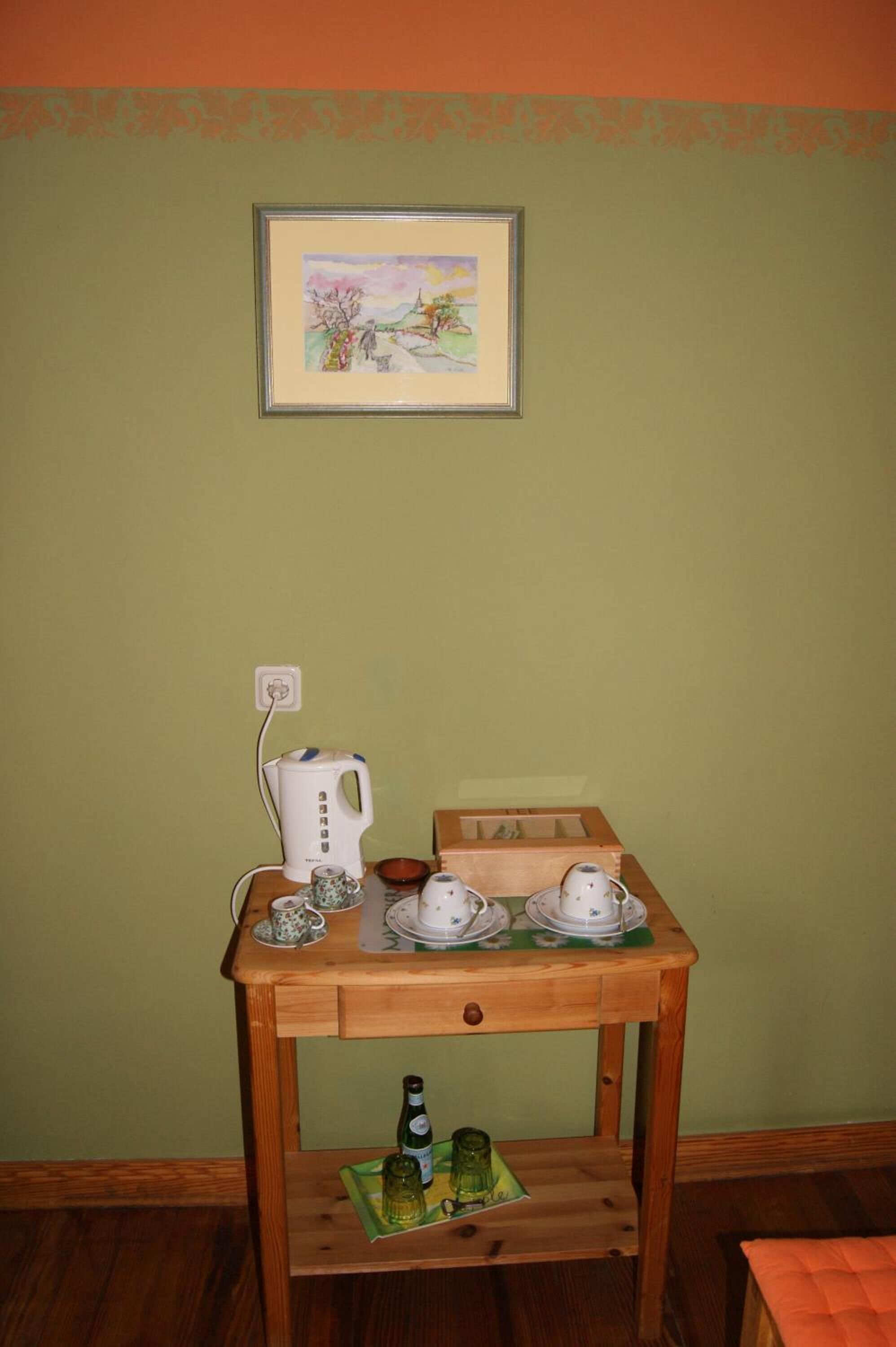 A wooden table with a kettle, teacups, saucers, and a bottle.