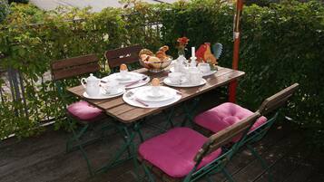 Un área de comedor al aire libre con una mesa de madera dispuesta para cuatro, rodeada de sillas de metal verde con cojines rosa.