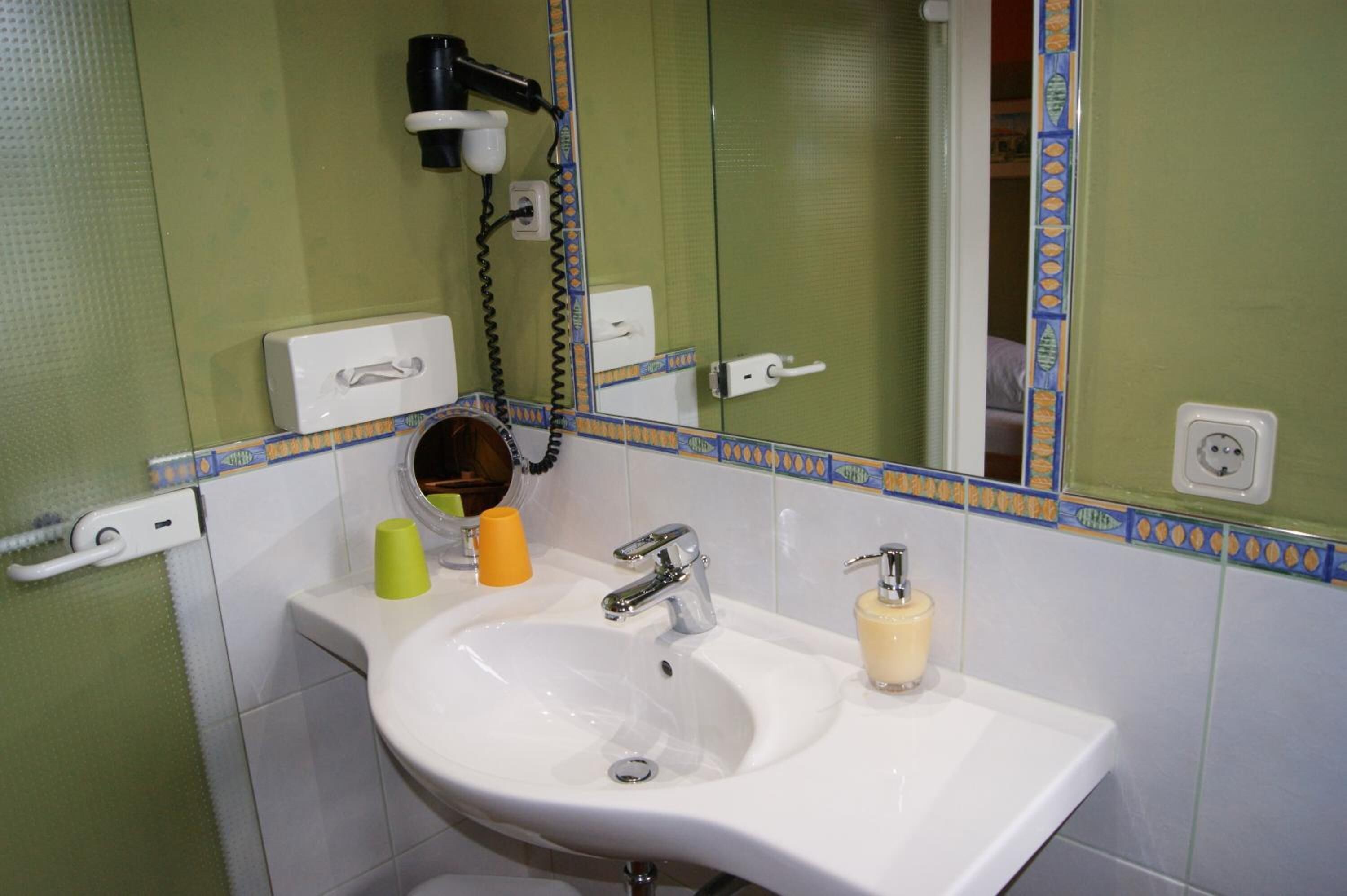Un baño con lavamanos blanco, un espejo, un secador de pelo y un perchero para toallas.