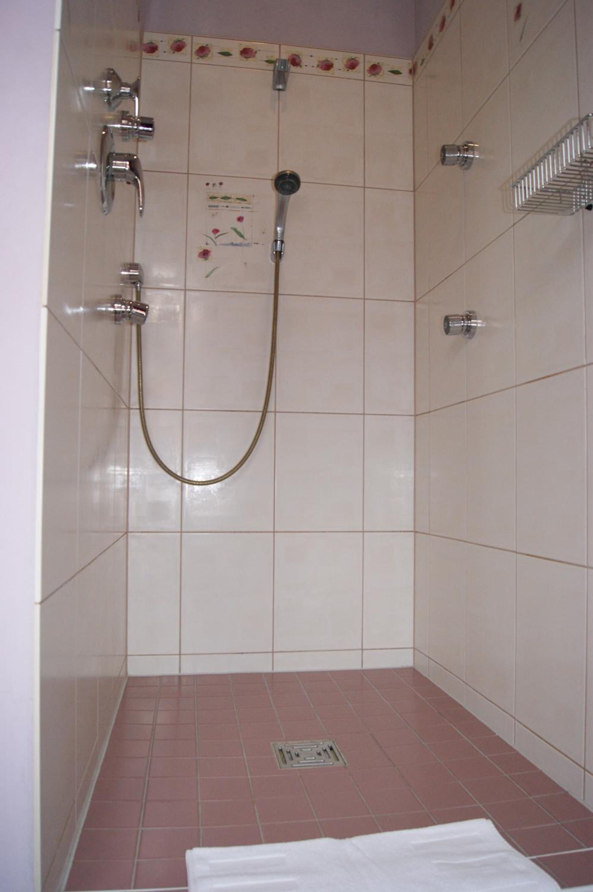 Un baño con ducha, secamanos y piso de cerámica.