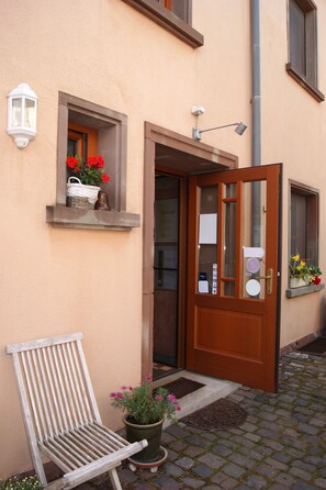 Una puerta de madera con un panel de vidrio, una silla blanca y una planta en maceta con flores rosas.