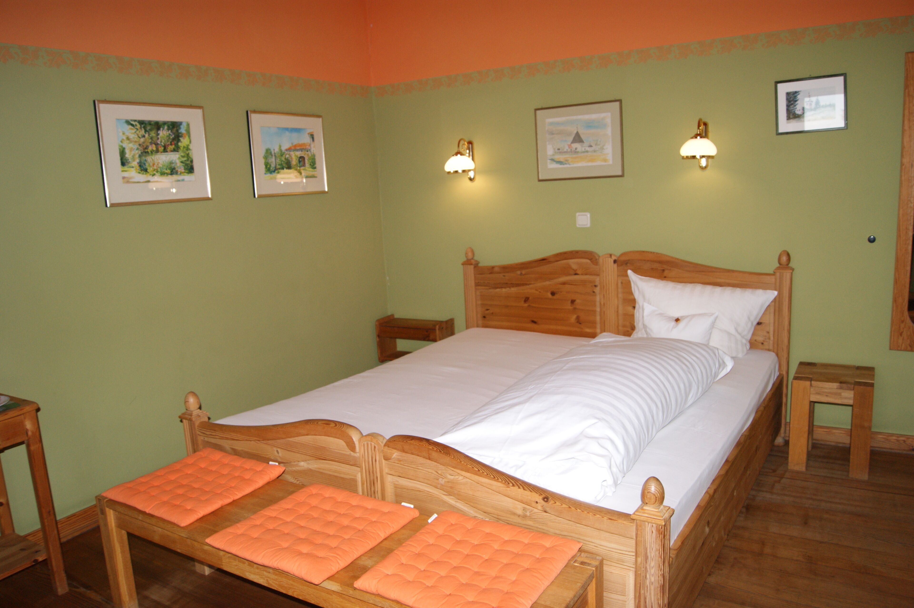 Une chambre avec un lit simple, une tête de lit en bois, deux tables de chevet et un petit tabouret en bois.
