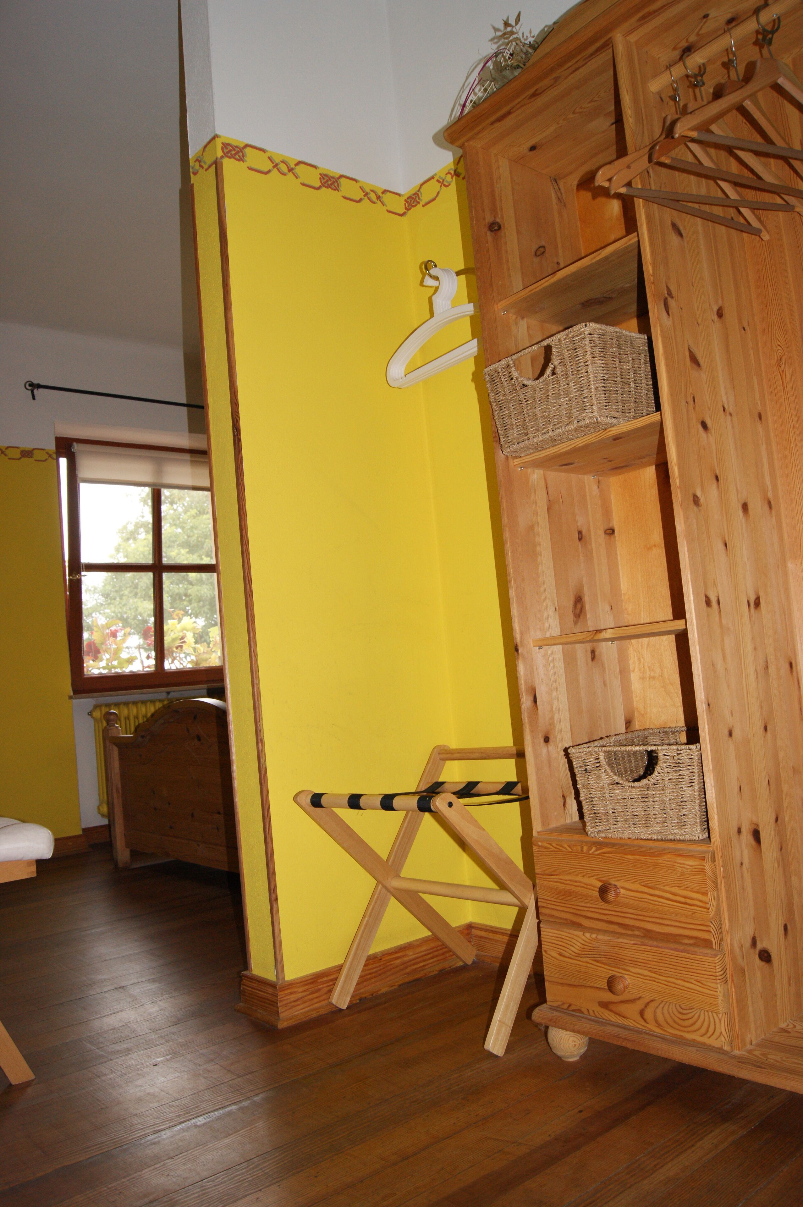 Una stanza con un armadio in legno contenente ceste, una sedia in legno e una finestra vista alberi.