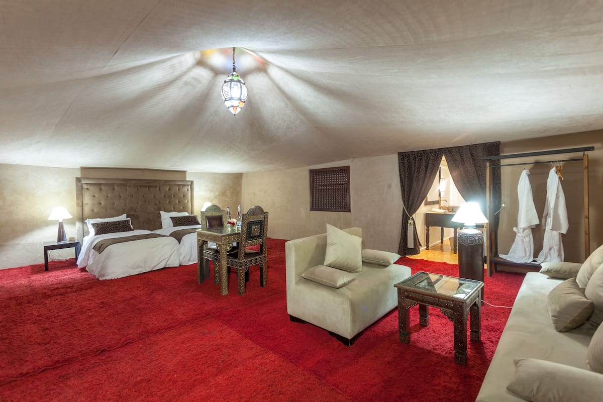 A hotel room with a red carpet, a bed, a sofa, a table, and a wardrobe.