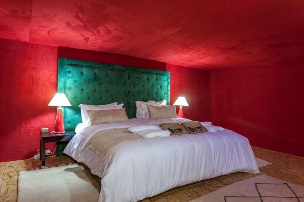 A bedroom with a green upholstered headboard, white bedding, two bedside tables with lamps, and a patterned rug.