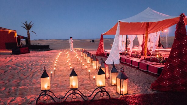 A desert wedding setup with a tent, lanterns, and a pathway leading to a seating area. - Lemnaouar Erg Camp (Rissani)