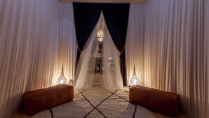 A corridor with draped curtains, a patterned carpet, and two illuminated wall sconces. - Lemnaouar Erg Camp (Rissani)