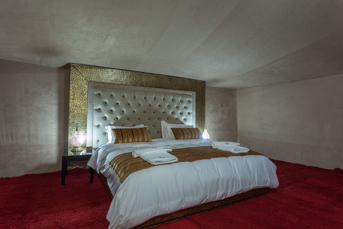 A large bed with a tufted headboard, white bedding, and a red carpet.