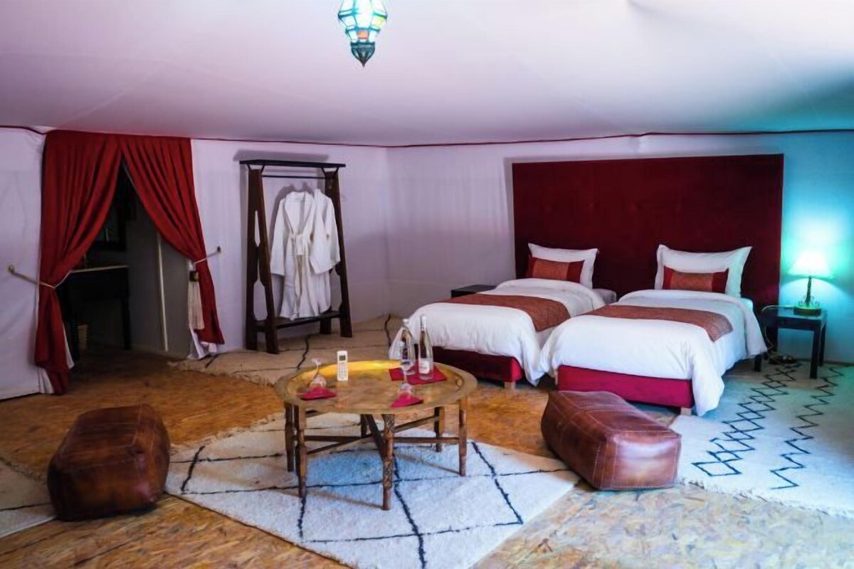 A bedroom with two beds, a wooden table, a robe rack, and a patterned rug.