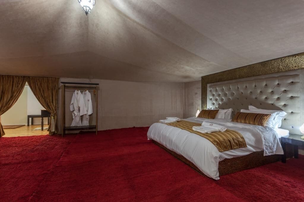 A spacious bedroom with a large bed, a red carpet, a wardrobe, and a mirror.