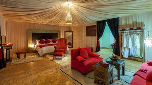 A luxurious room with a large bed, a red sofa, a wooden coffee table, and a chandelier. - Lemnaouar Erg Camp (Rissani)